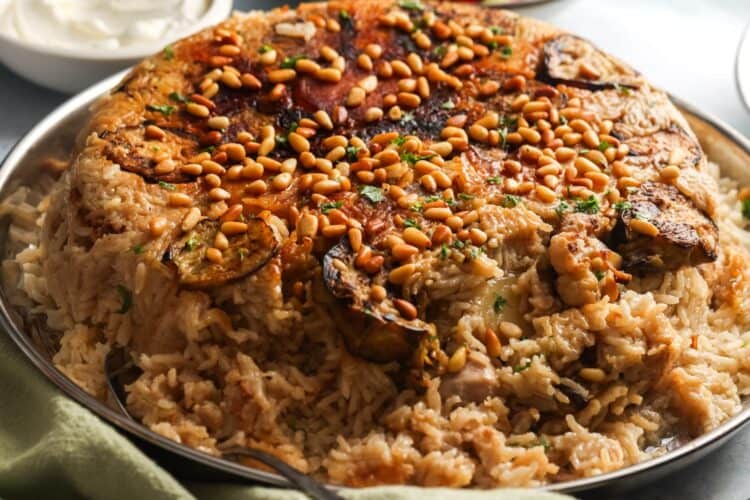 cooked maqluba, flipped over onto a large platter. on top are toasted pine nuts.