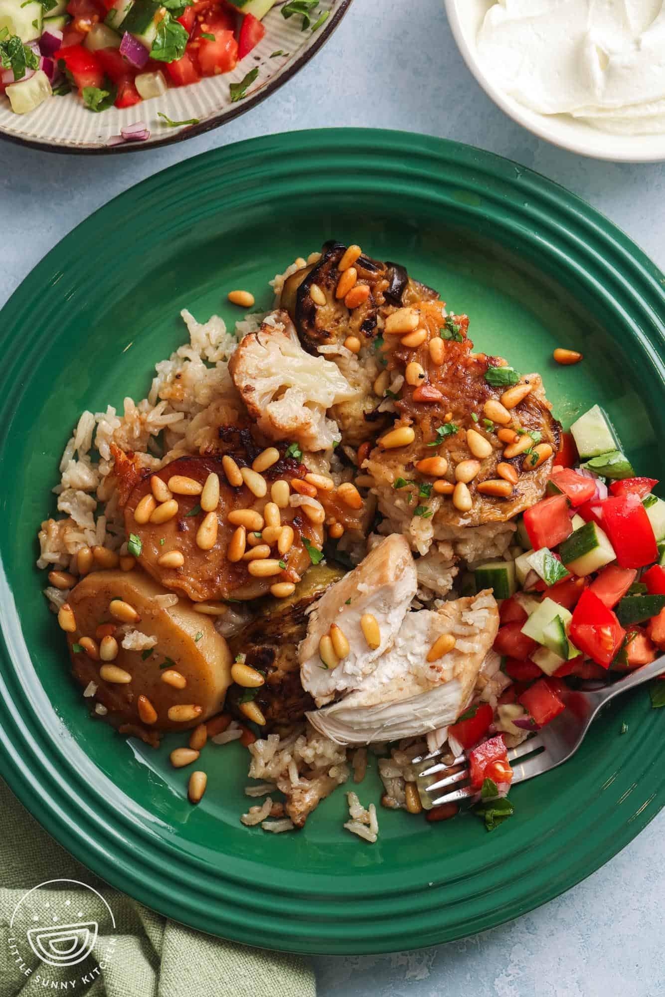 a dark green plate with a serving of maqluba with chicken and vegetables.