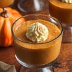 a footed glass dish of pumpkin pudding topped with fresh whipped cream and ground cinnamon