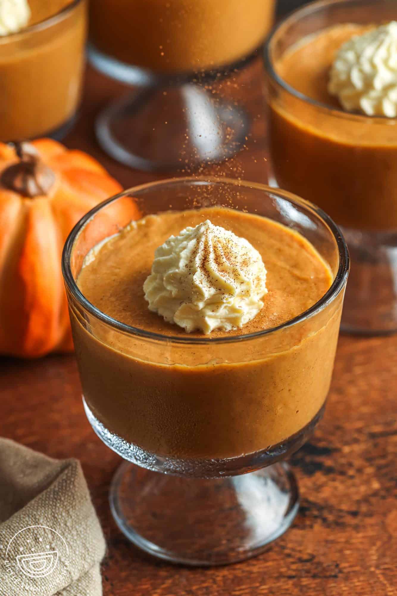 a footed glass dish of pumpkin pudding topped with fresh whipped cream and ground cinnamon