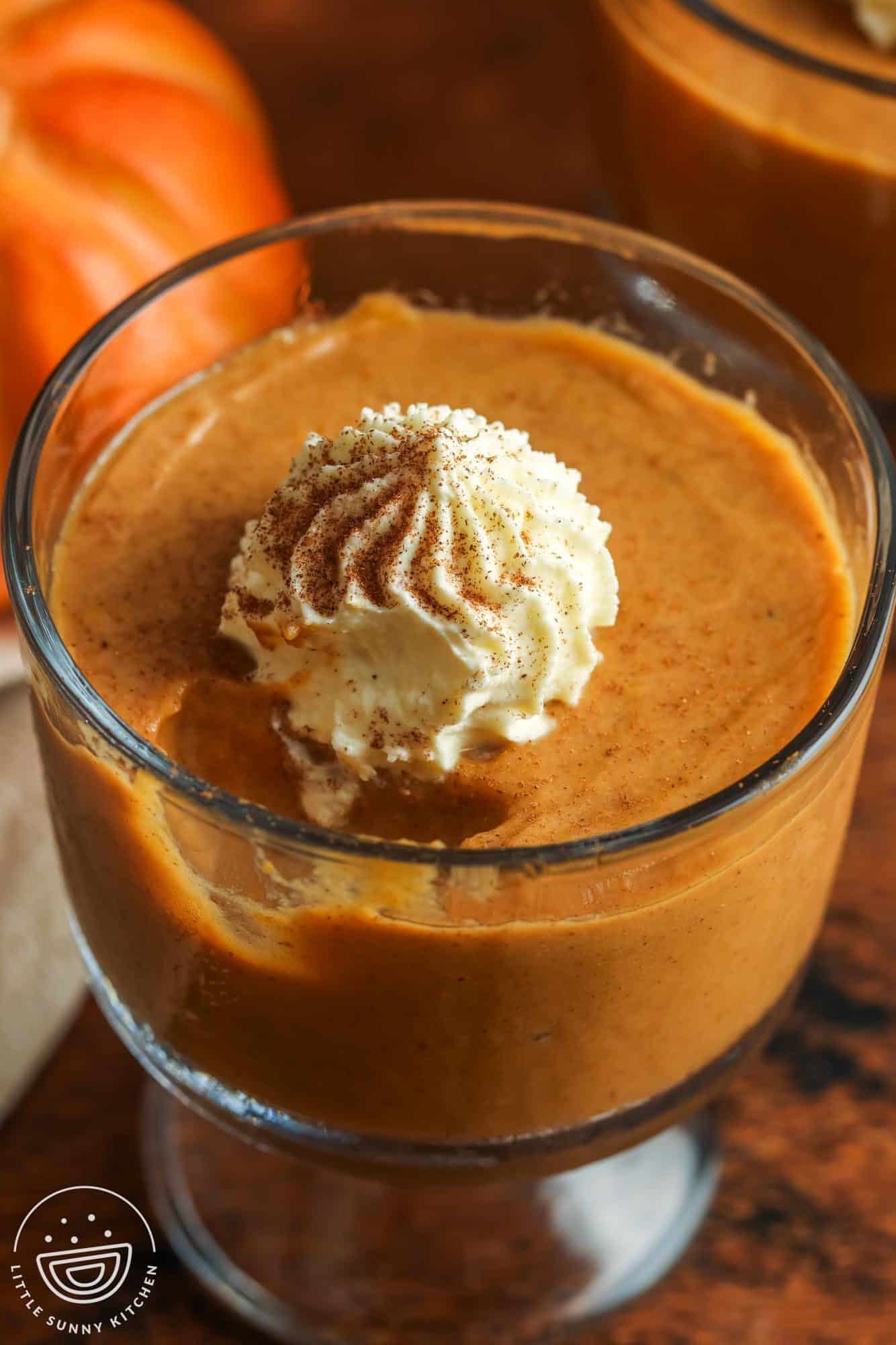 closeup of a small glass bowl of pumpkin pudding topped with cinnamon whipped cream. A bite has been taken.