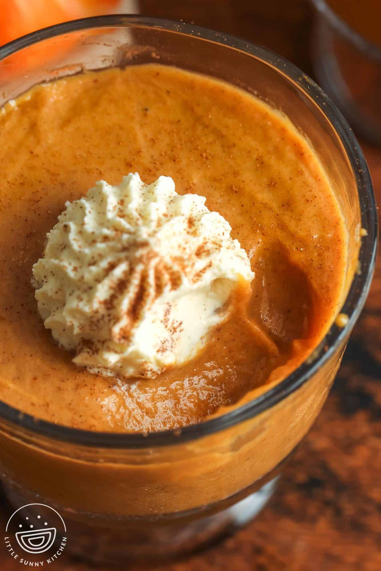 overhead closeup view of homemade pumpkin pudding with whipped cream, sprinkled with cinnamon.