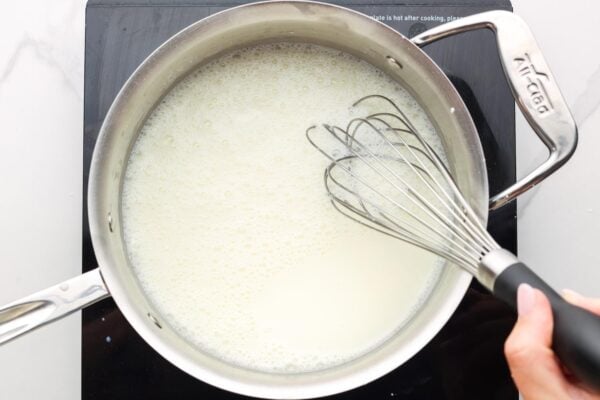 cornstarch, sugar, and milk cooking in a saucepan while stirred with a wire whisk.