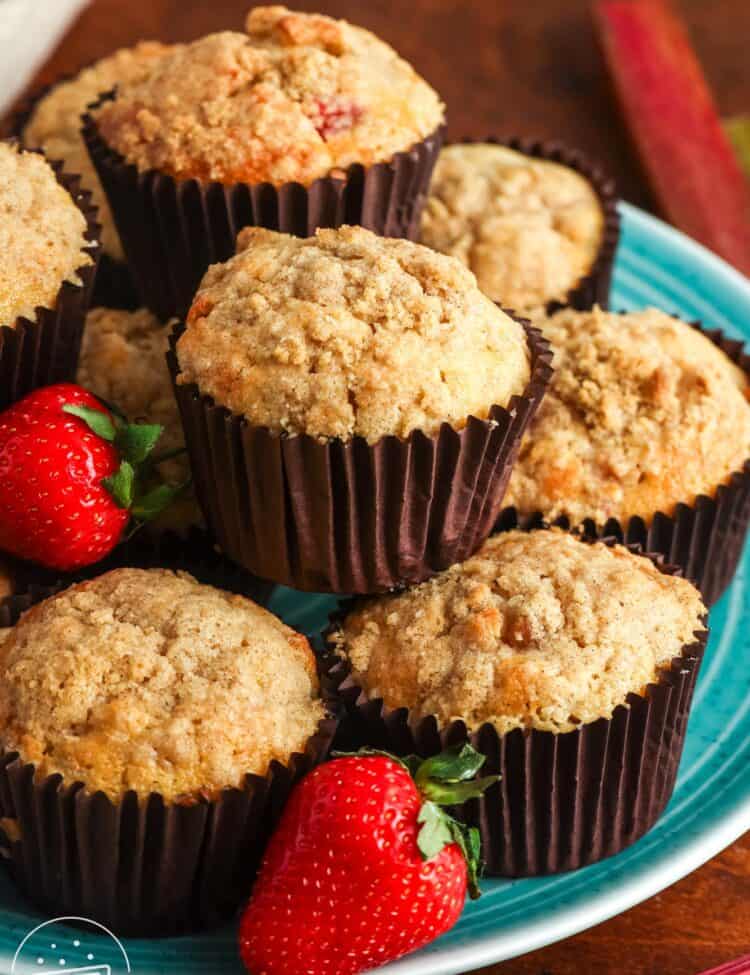 A teal platter stacked with two layers of strawberry rhubarb muffins. The plate is garnished with fresh berries.