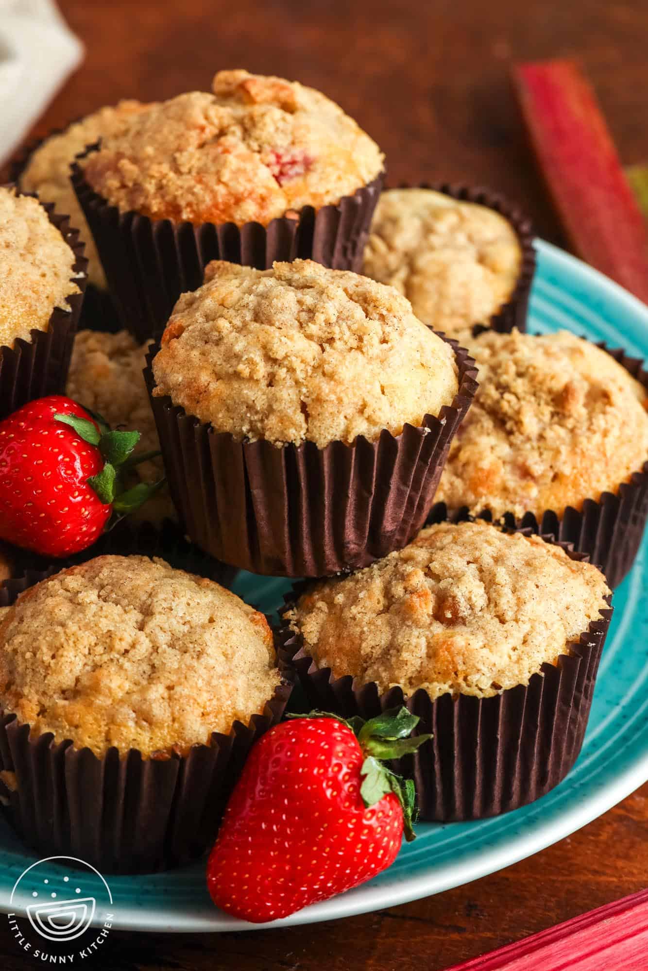 A teal platter stacked with two layers of strawberry rhubarb muffins. The plate is garnished with fresh berries.