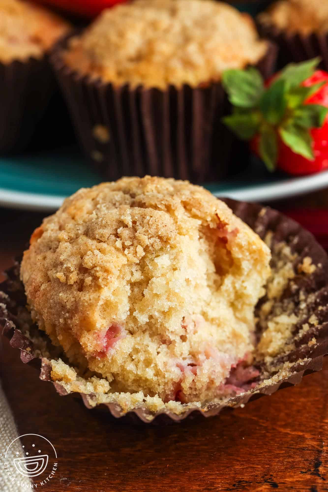 a strawberry rhubarb muffin unwrapped and with a bite taken. The interior texture of the muffin is soft, fluffy, and moist.