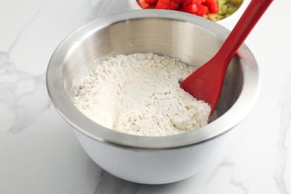 a metal bowl of flour. A red spoon is mixing it with salt and baking powder.