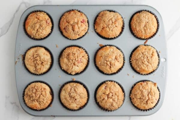 Baked strawberry rhubarb muffins with domed tops in a cupcake tin, viewed from overhead.