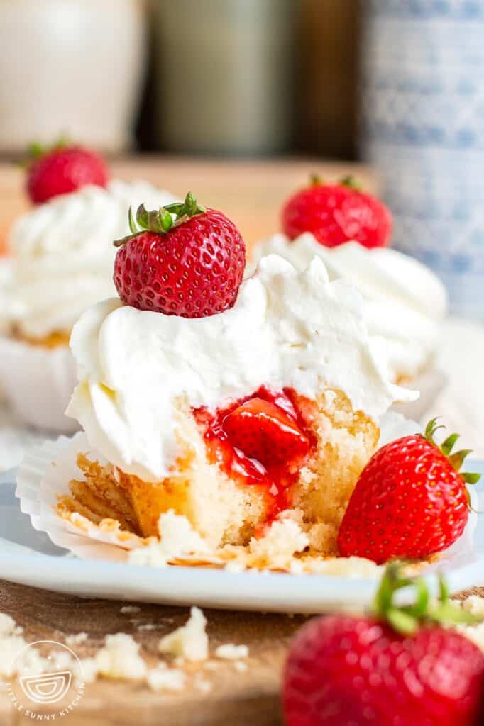 Two strawberry stuffed cupcakes on a plate. Each is topped with fluffy whipped cream and a whole strawberry.