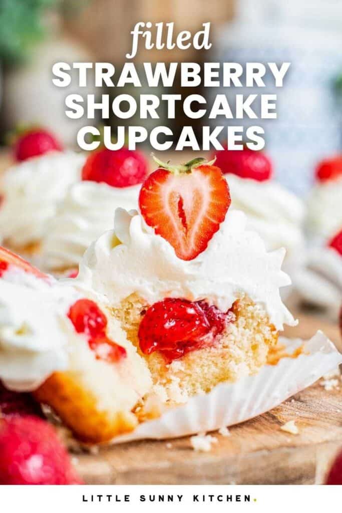 A vanilla cupcake with whipped cream frosting cut in half to show that it's filled with strawberries. Text overlay says "filled strawberry shortcake cupcakes"