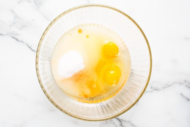 eggs, oil, and sugar in a glass mixing bowl that is on a marble surface, viewed from overhead.