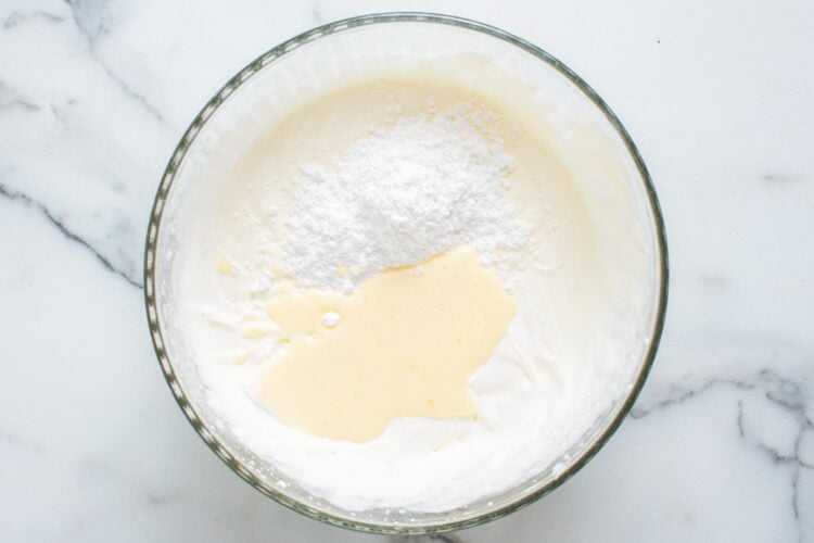 gelatin and powdered sugar added to a bowl of cream that has been whipped to soft peaks.
