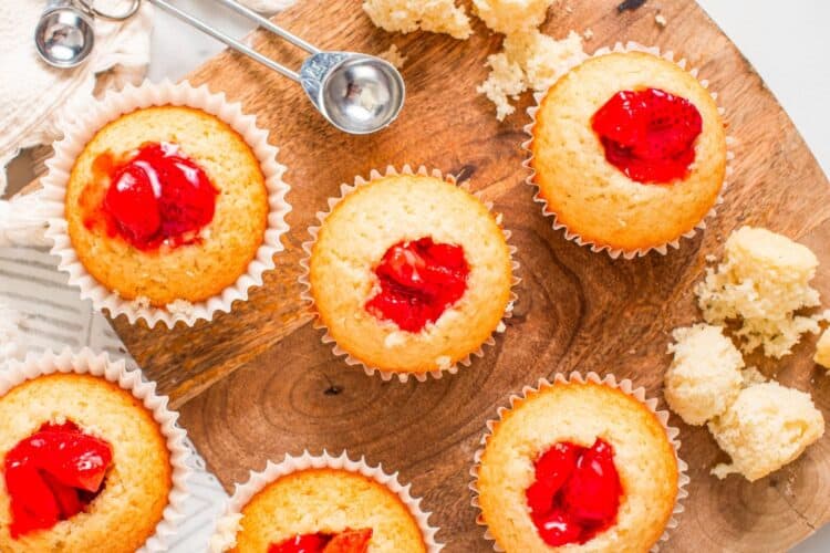 cupcakes on a wooden board. Each has had a hole made in the center with a metal teaspoon, and the hole has been filled with strawberry compote.
