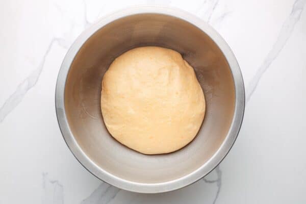 sweet potato dinner roll dough in an oiled metal mixing bowl.
