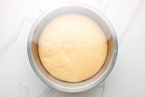 a bowl of risen sweet potato dinner roll dough that is covered in plastic wrap.
