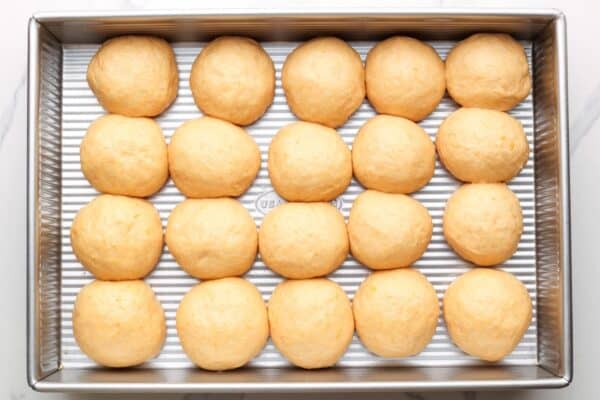 Sweet potato dinner roll dough balls added to a metal baking pan.