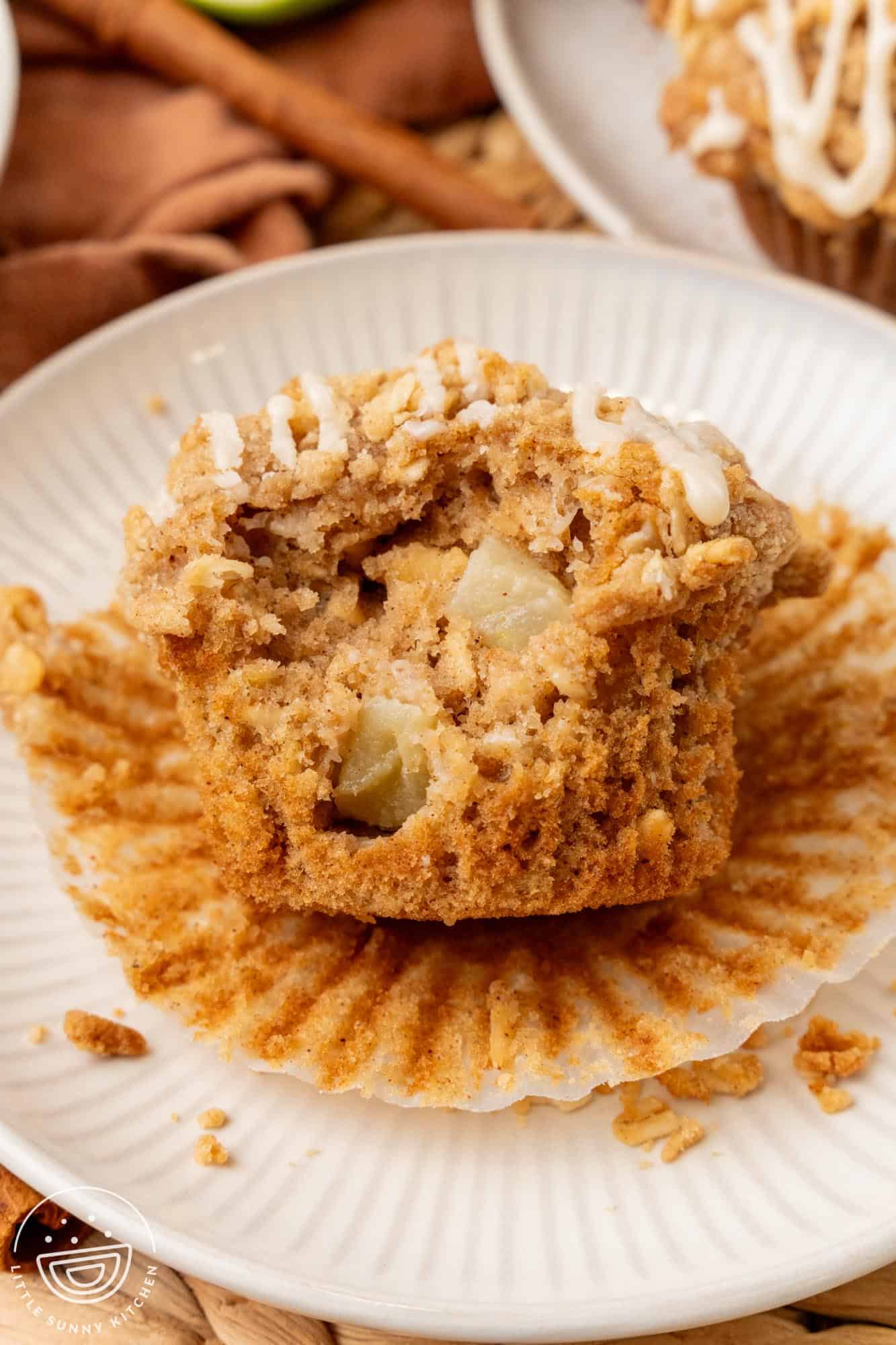 an apple oat muffin removed from it's paper. A bite has been taken to show the apple pieces inside.
