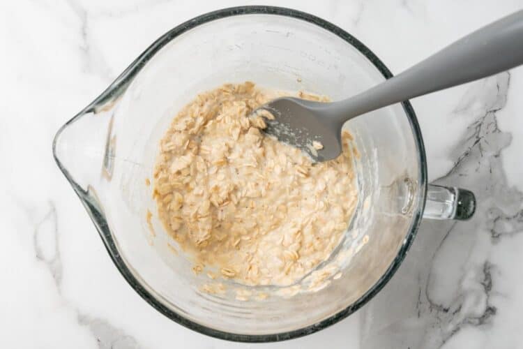 oats, applesauce, and milk stirred together in a large glass bowl with a gray spatula.