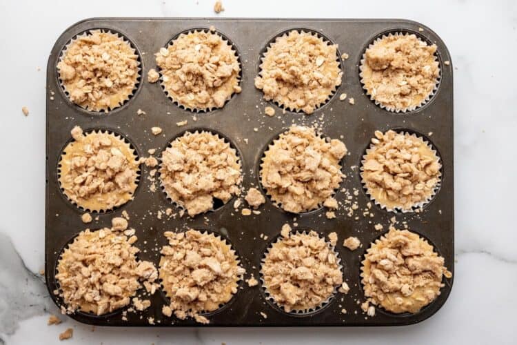 crumble topping added to apple muffins in a muffin pan.