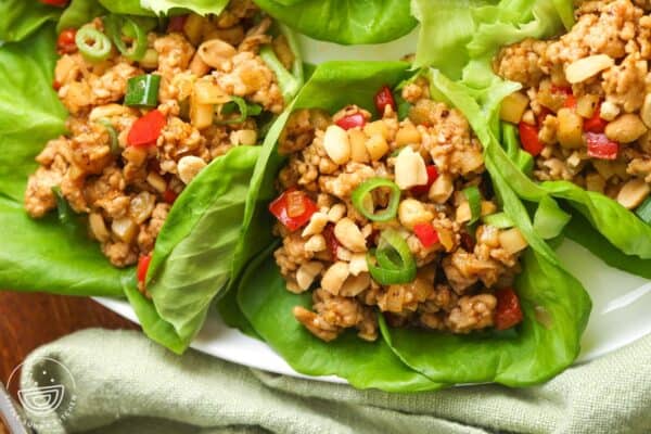 Asian chicken lettuce wraps with peppers and peanuts, sitting on a white plate.