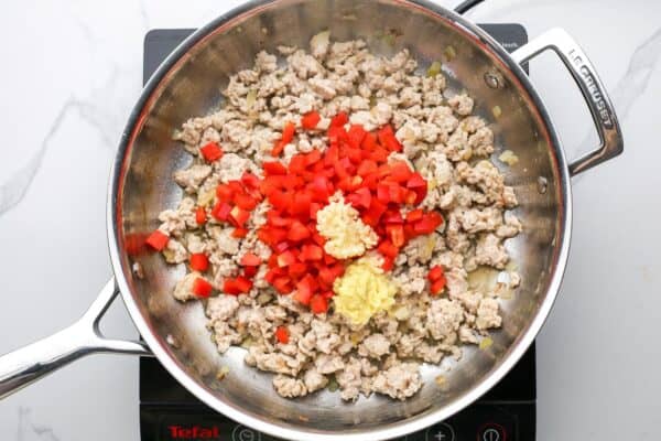 red peppers, garlic, and ginger added to a skillet of cooked ground chicken.
