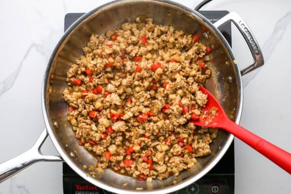 filling for asian chicken lettuce wraps, cooking in a skillet, stirred with a red spoon.