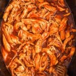 bbq crockpot pulled chicken with two forks in a black pot.