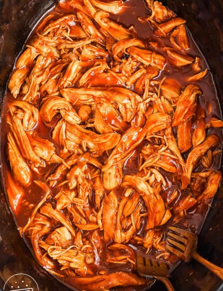 bbq crockpot pulled chicken with two forks in a black pot.