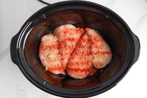 chicken breasts in a crockpot liner seasoned with spices.