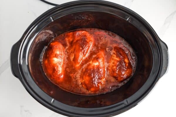 four bbq chicken breasts cooking in a crockpot.