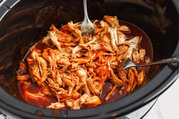 bbq chicken pulled apart by two forks in a slow cooker.