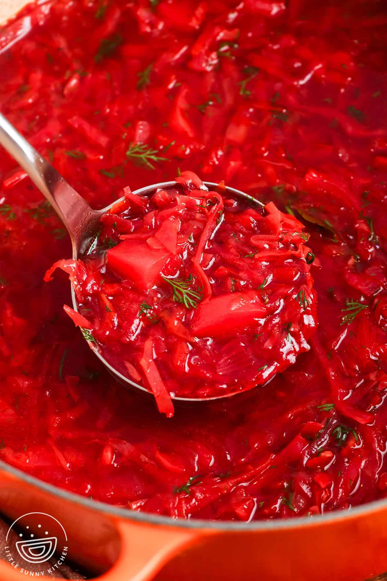 closeup of a pot of borscht soup showing the carrots, beets, and potatoes in a deep red broth.