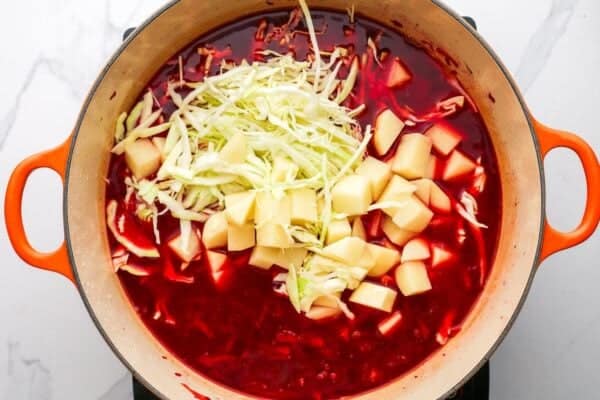 cabbage and potatoes added to beet soup in a dutch oven