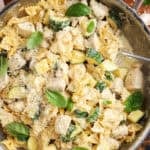 creamy chicken and zucchini pasta served from a stainless steel skillet with a spoon. The pasta is garnished with whole basil leaves and grated parmesan.