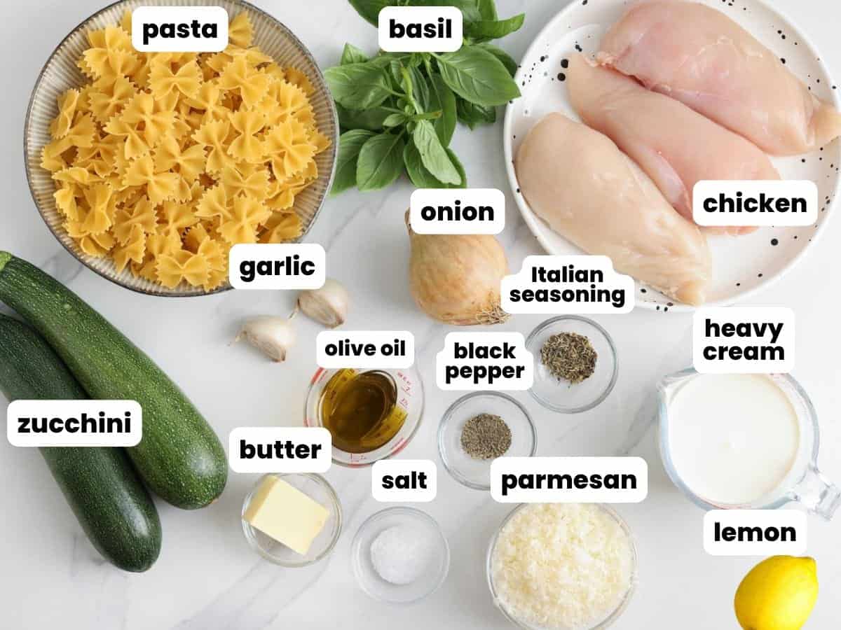 ingredients for making a pasta dish with zucchini, chicken breasts, and a creamy sauce. All of the ingredients are measured into small bowls, arranged on a counter.