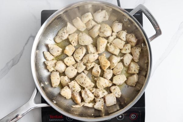 bite-sized pieces of chicken searing in a stainless steel skillet in oil.