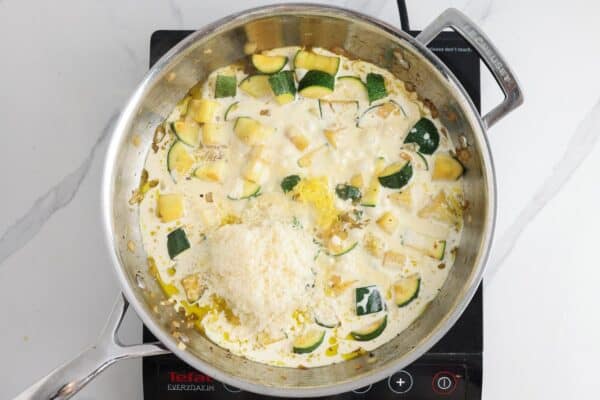 Cream and parmesan cheese added to sauteed veggies to create a sauce in a pan.