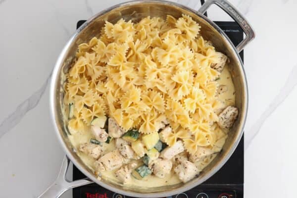 cooked bowtie pasta added to chicken and zucchini in a creamy sauce.