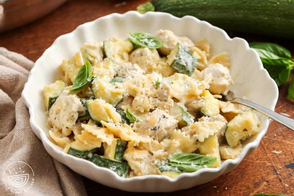 A bowl of Creamy Chicken Zucchini Pasta and a fork, placed on a wooden table top.