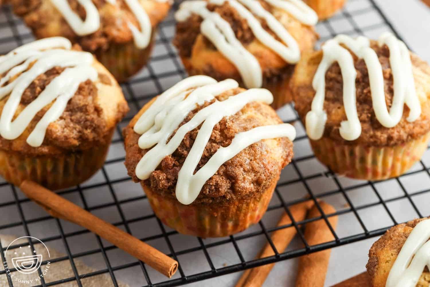 Angle view of cinnamon roll muffins topped with frosting, sitting on a wire rack.
