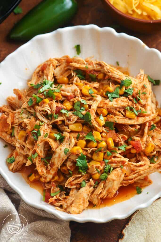 a white fluted bowl filled with shredded salsa chicken, garnished with chopped cilantro.