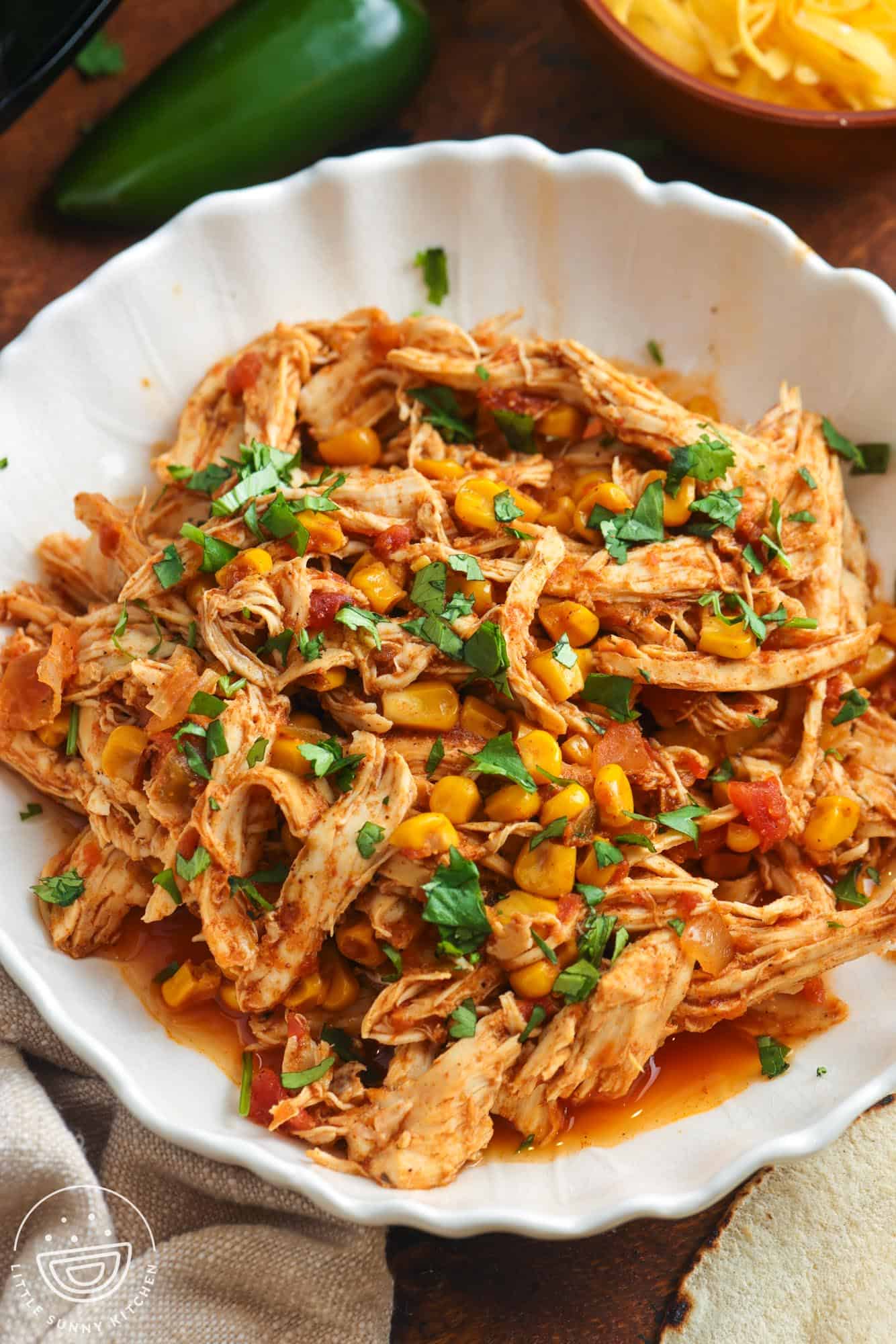 a white fluted bowl filled with shredded salsa chicken, garnished with chopped cilantro.