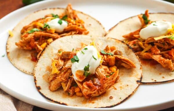 three toasted tortillas on a platter, topped with crockpot salsa chicken, cheese, and sour cream.