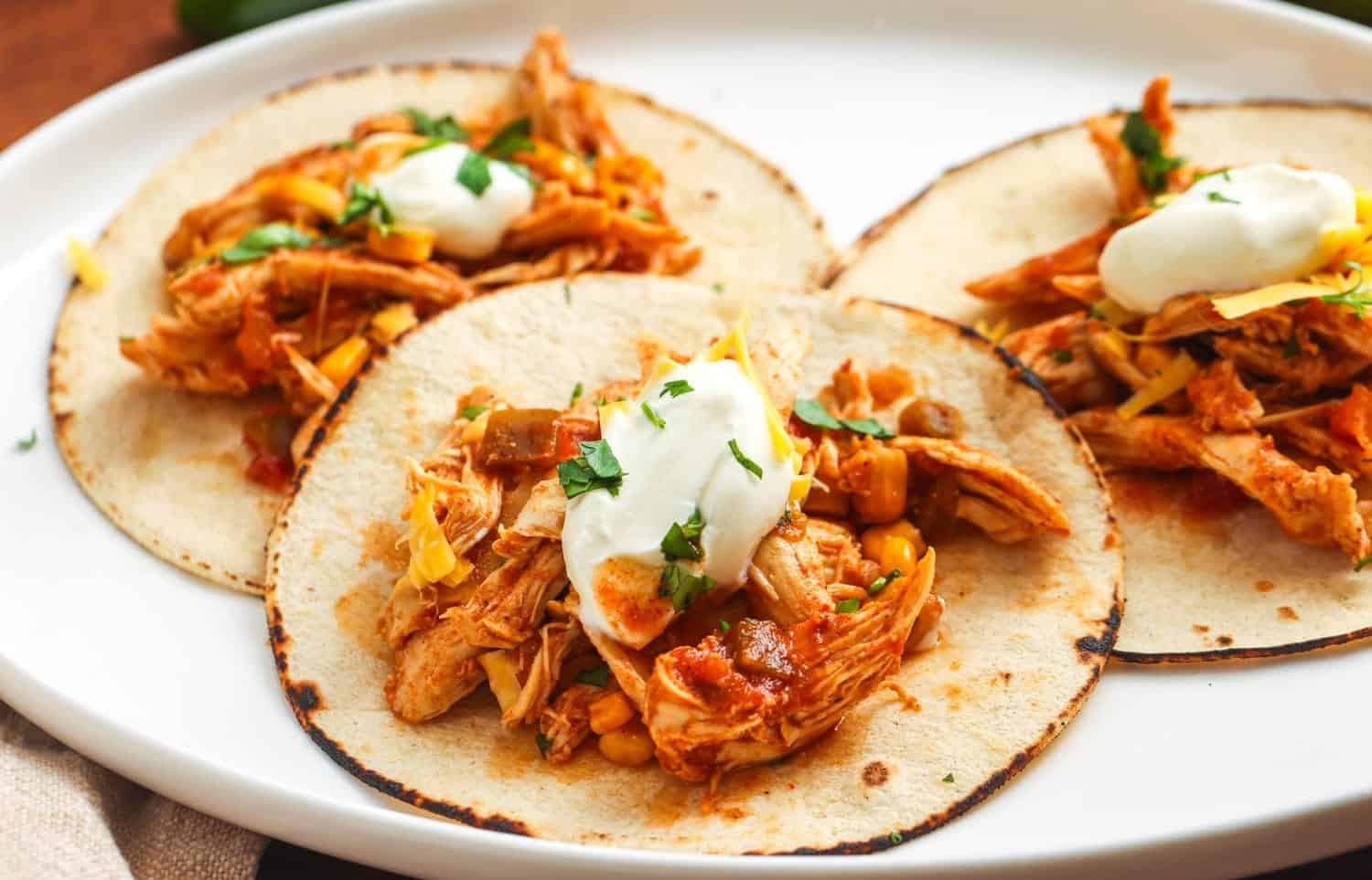 three toasted tortillas on a platter, topped with crockpot salsa chicken, cheese, and sour cream.