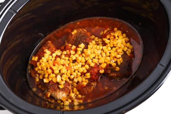 cooked salsa chicken breasts topped with corn in a crockpot.