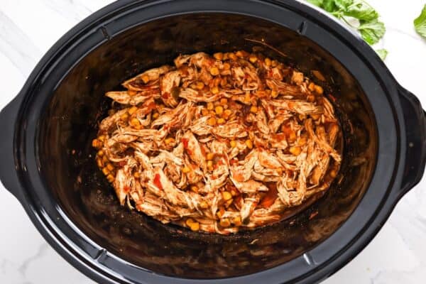 shredded crockpot salsa chicken inside of a black oval crockpot.