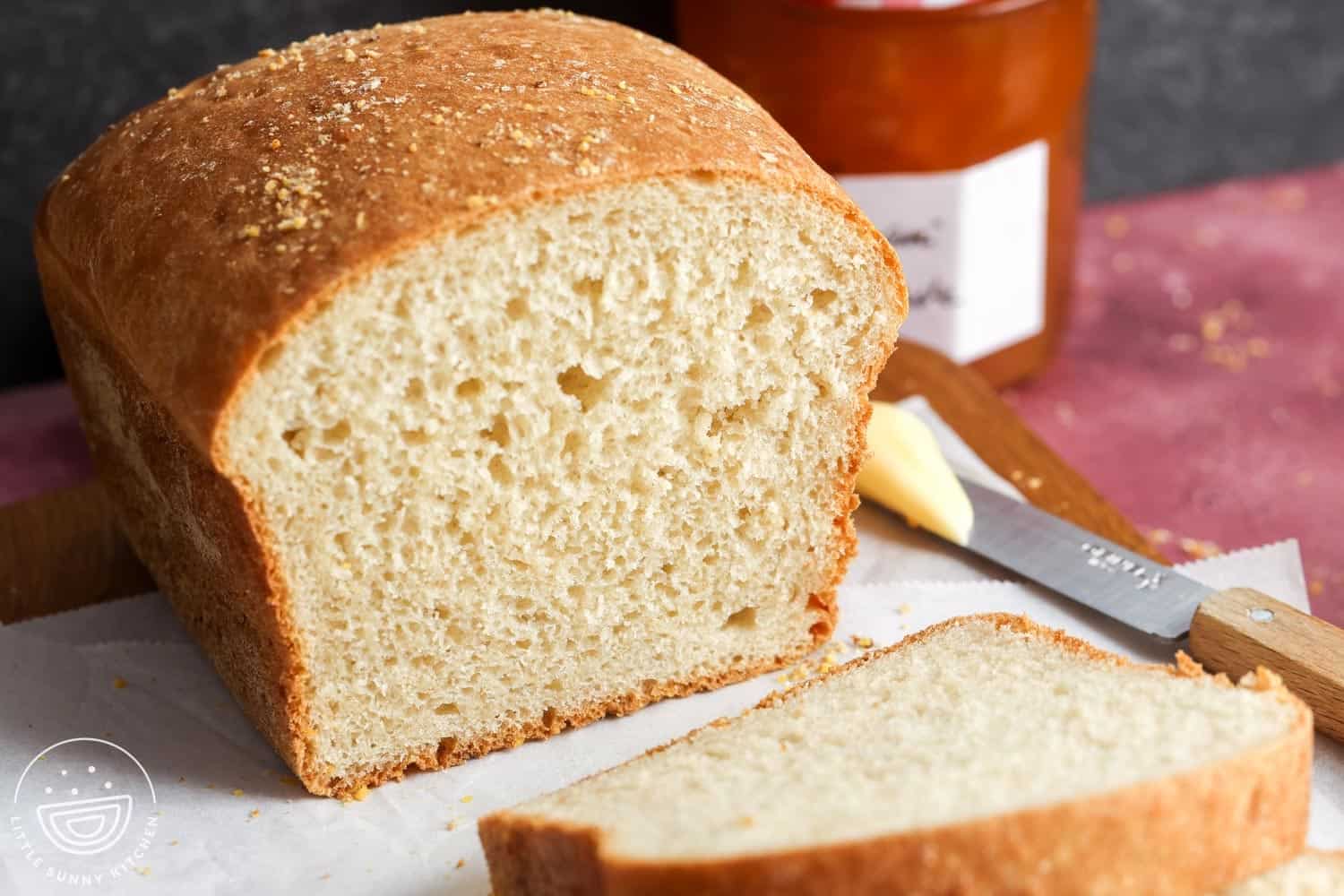 Freshly baked loaf of English muffin bread on a cutting board, with one slice cut and a butter knife beside it, showing its airy, open crumb texture.