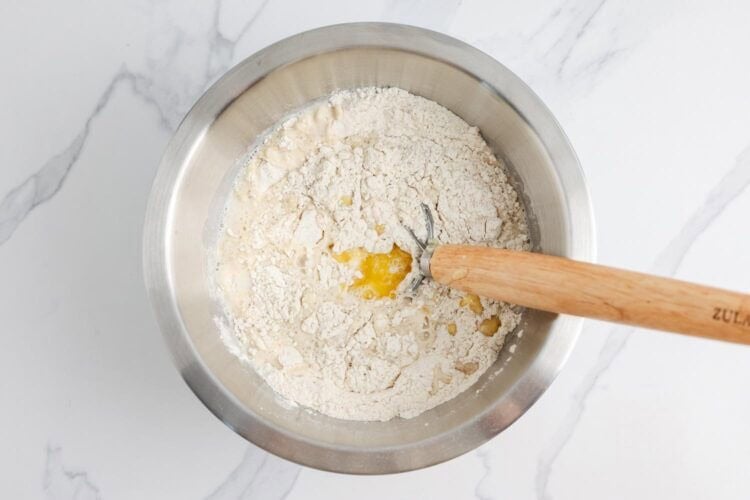 water, melted butter, milk, and honey added to dry ingredients in a metal bowl, stirred with a bread whisk.