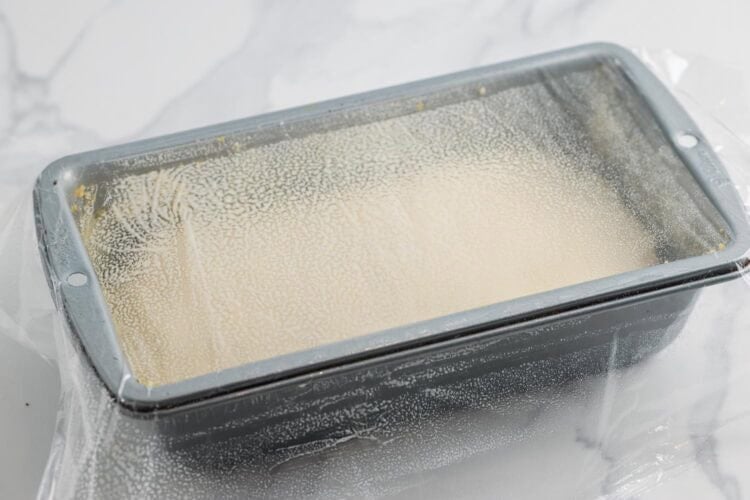 dough rising in a metal loaf pan, covered with greased plastic wrap.