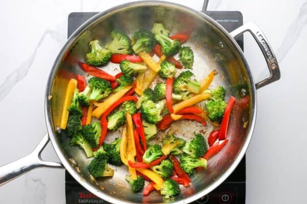broccoli florets and sliced bell peppers stir fried in a stainless steel skillet.